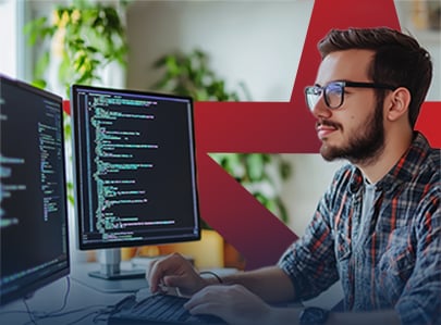 A young man working on code on duel computer setup.